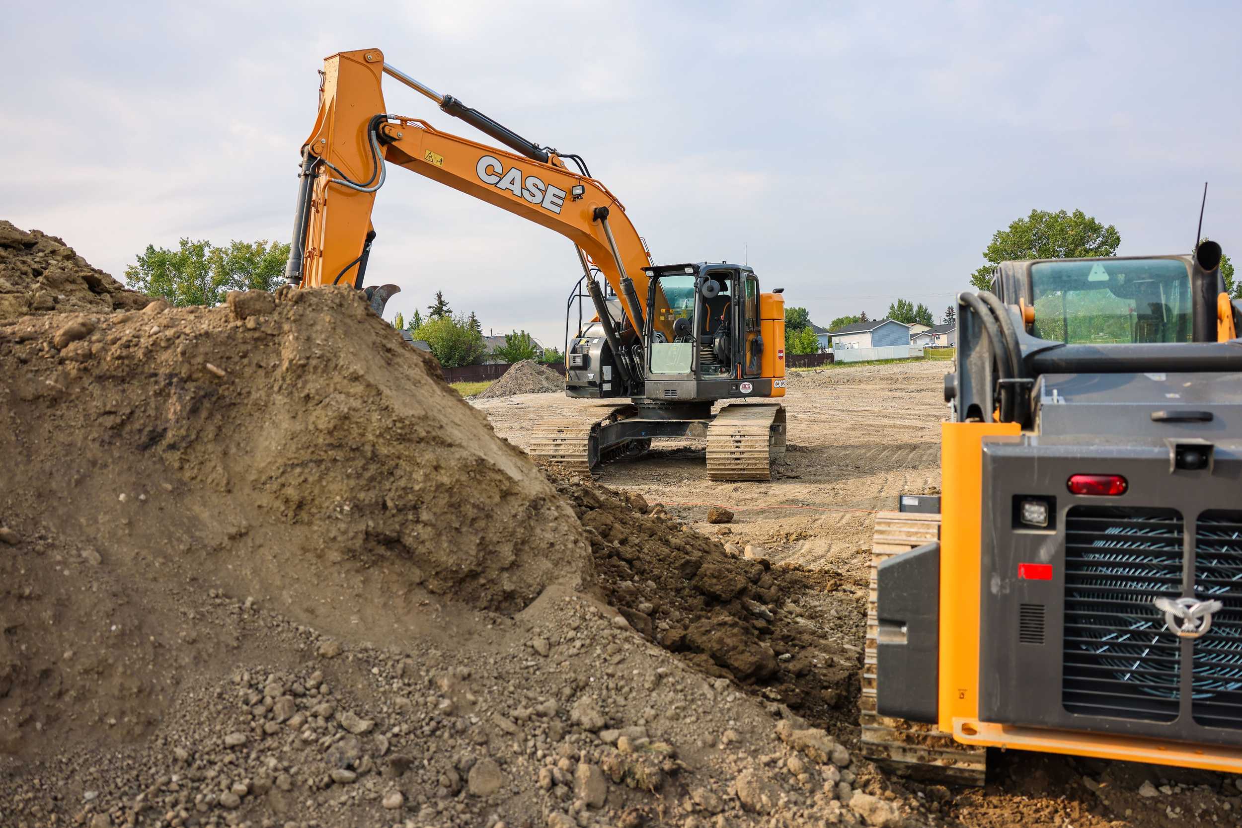 Large construction equipment, with pile of dirt in foreground and construction site in background